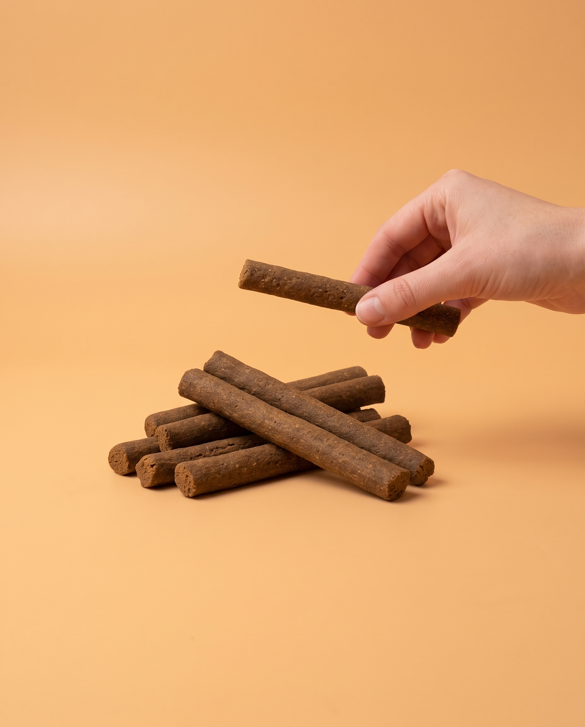 Sfeerfoto: hand biedt een frikandel met kip aan tegen een abrikooskleurige studioachtergrond