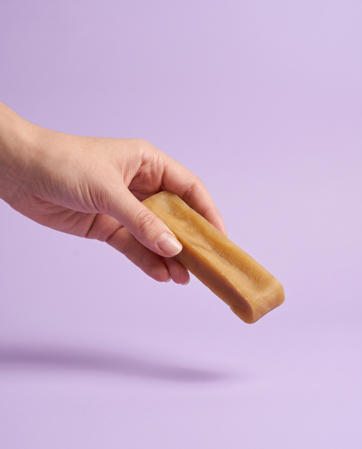 Sfeerfoto: hand biedt een yakkaas staafje aan tegen een lila studioachtergrond