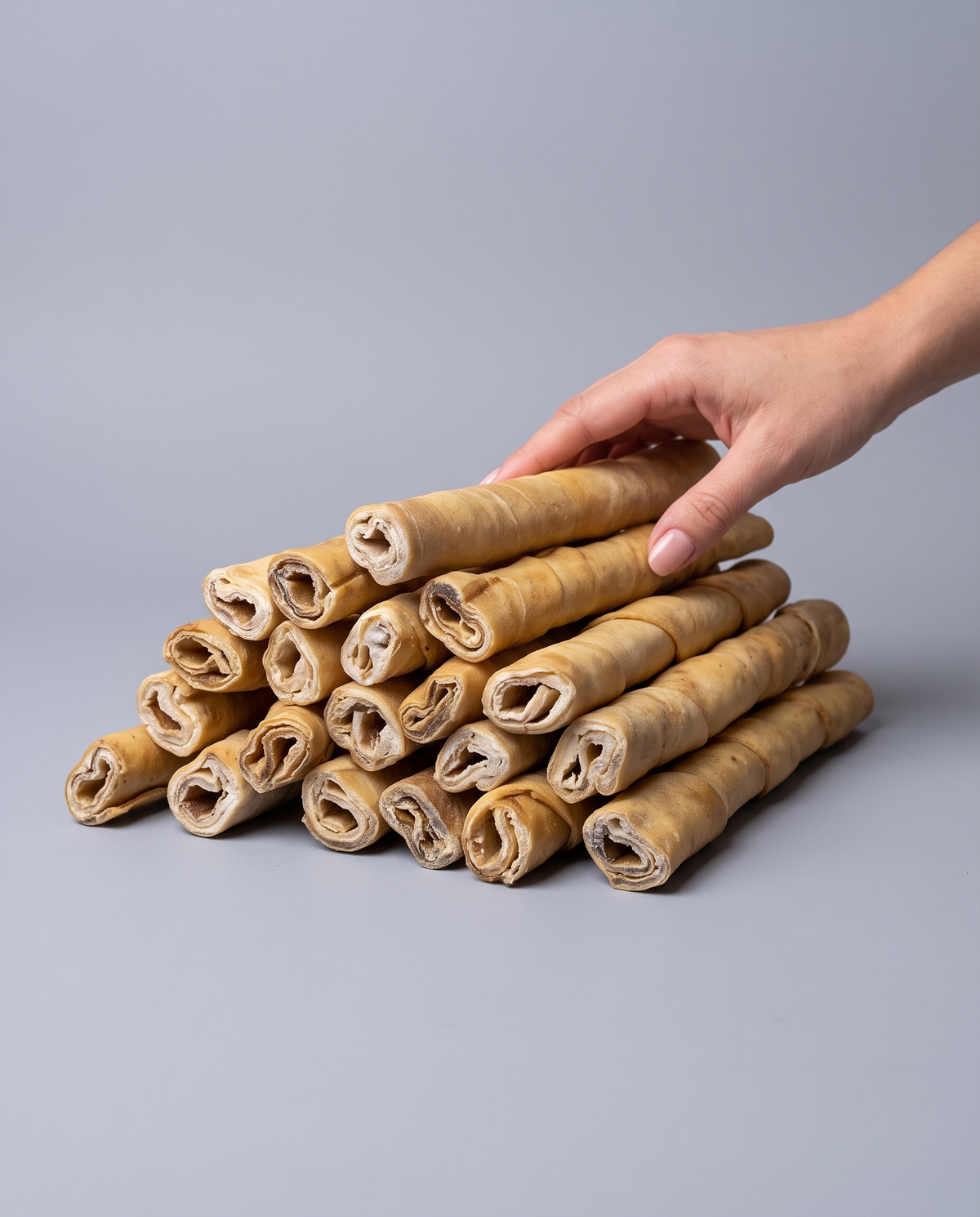 Sfeerfoto: stapel van meerdere rollen runderkophuid (1000 gram) met hand, tegen een grijze studioachtergrond