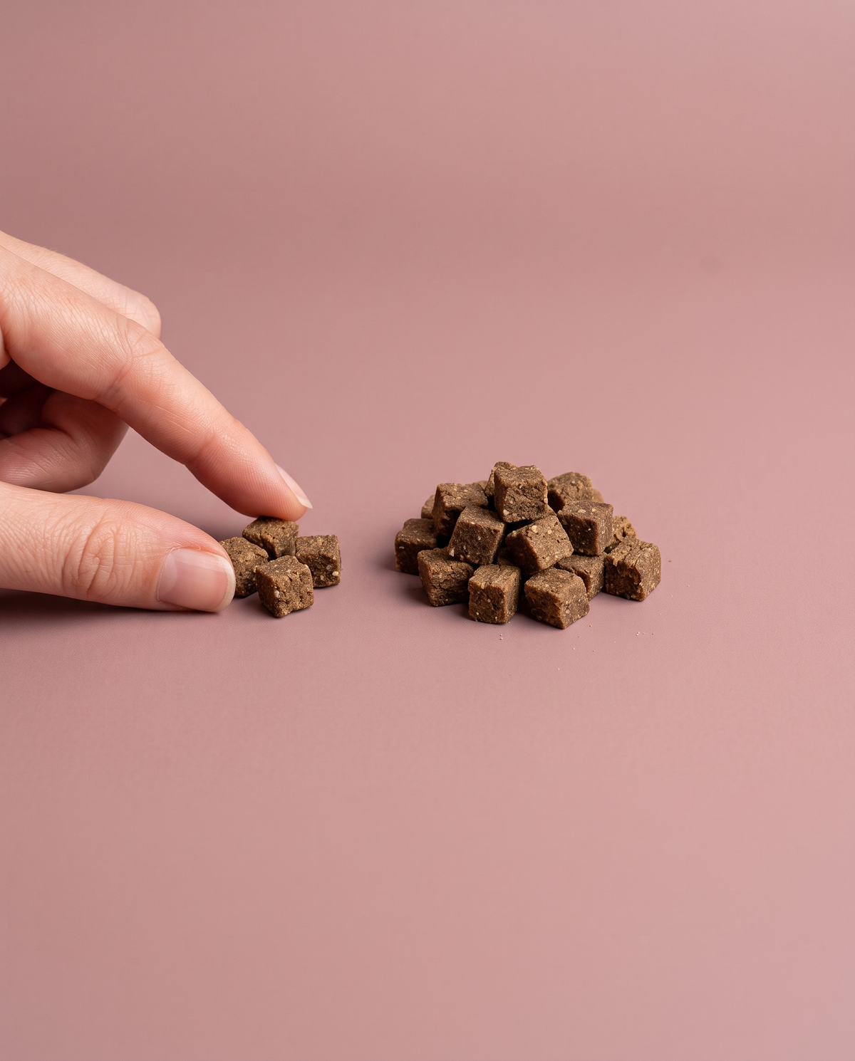 Sfeerfoto: kleine hoeveelheid mini trainers met hert (200 gram) met hand, tegen een oudroze studioachtergrond