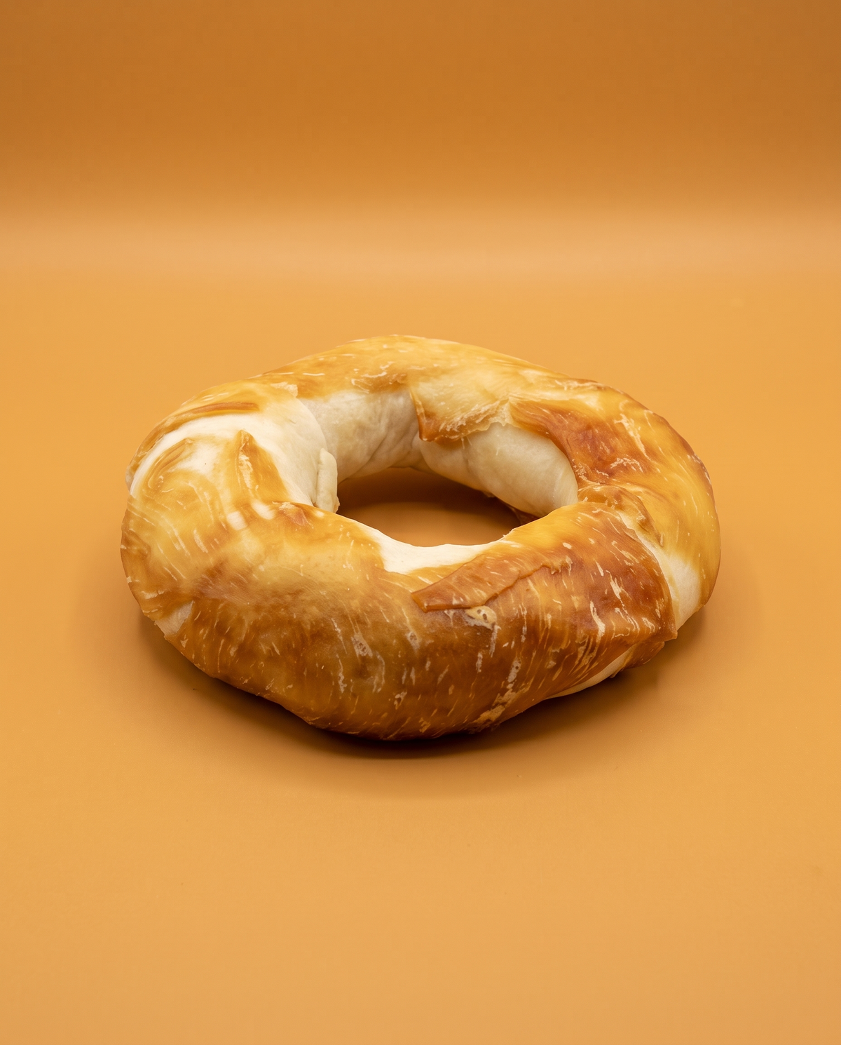 Sfeerfoto: 1 groot rawhide donutje met kip XL (170-190 gram), tegen een amberkleurige studioachtergrond
